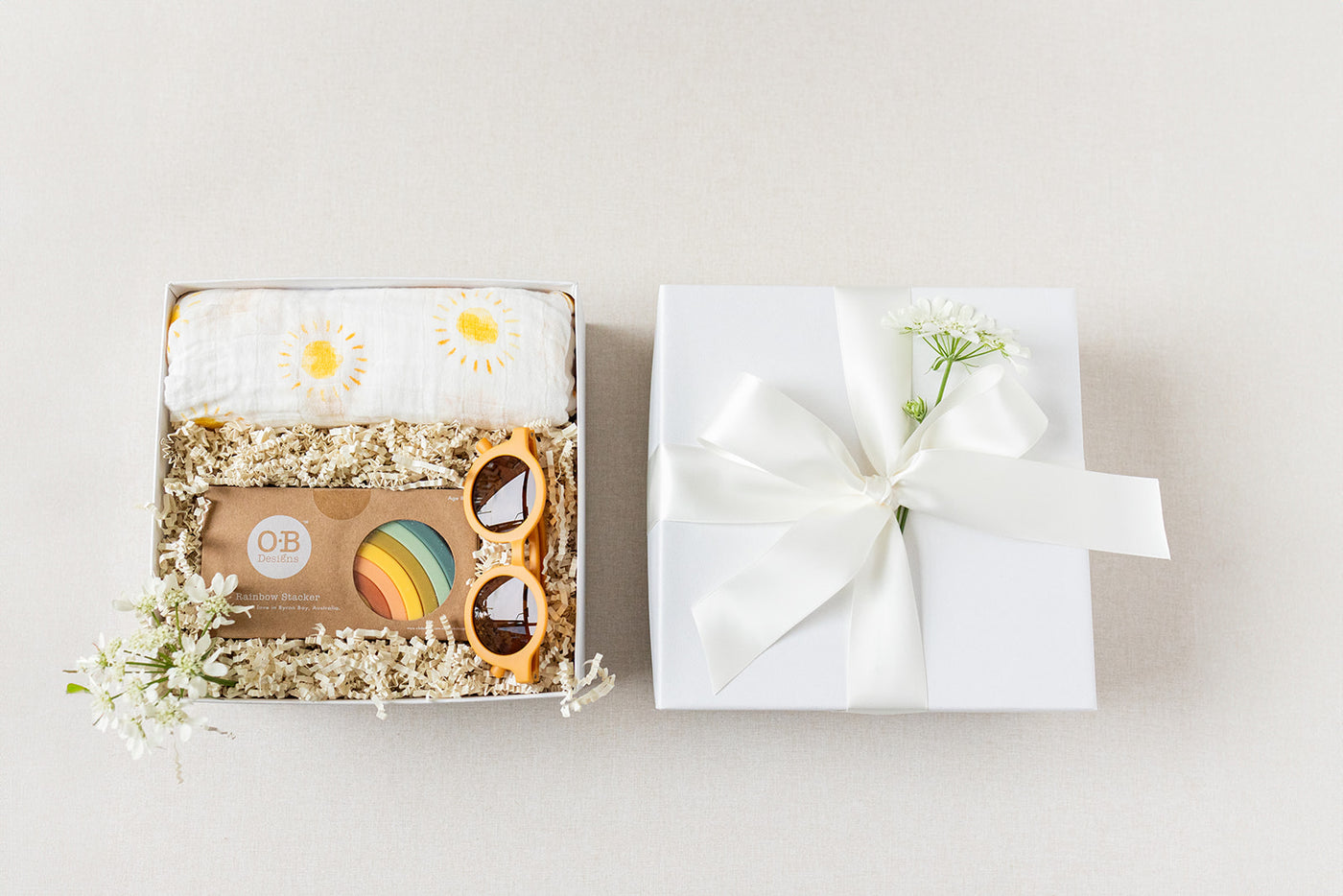 The Duckbill - New Baby Gift by LUX BOX co. includes a sun-adorned cotton swaddle, wooden toys, a card, and a silicone rainbow stacking toy. It comes beautifully packaged with a white ribbon and flower—an ideal present for any new arrival.