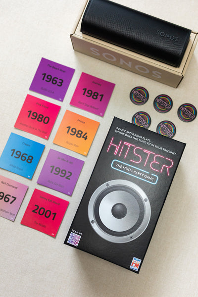 A LUX BOX co. Tune In & Play On set features a speaker in its box, a music game party box, colorful year cards from 1963-1981, and round tokens arranged on a light surface, all ready for a fun song battle.