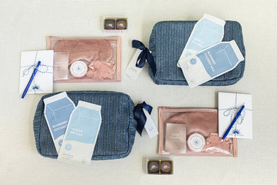 Gift sets include a blue textured bag, a pink sleep mask, habit tracker, pen, nourishing oat milk formula, and two small boxes with a shell design, arranged on a light background.