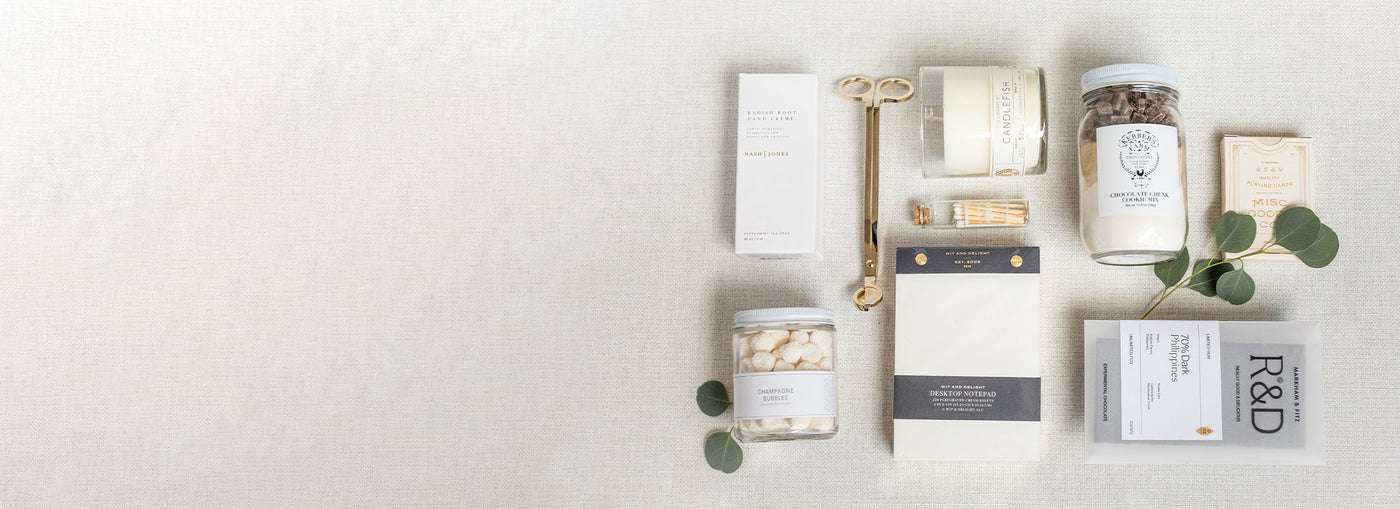 A neatly arranged flat lay of various packaged items, including tea, matches, a candle, and decorative leaves on a neutral background. Perfect for a gifting company specializing in corporate gifts or thoughtful offerings for social events.