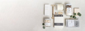 A neatly arranged flat lay of various packaged items, including tea, matches, a candle, and decorative leaves on a neutral background. Perfect for a gifting company specializing in corporate gifts or thoughtful offerings for social events.
