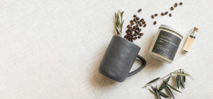 gray mug, coffee beans, white candle with gray label, matches in glass jar, decorative greenery