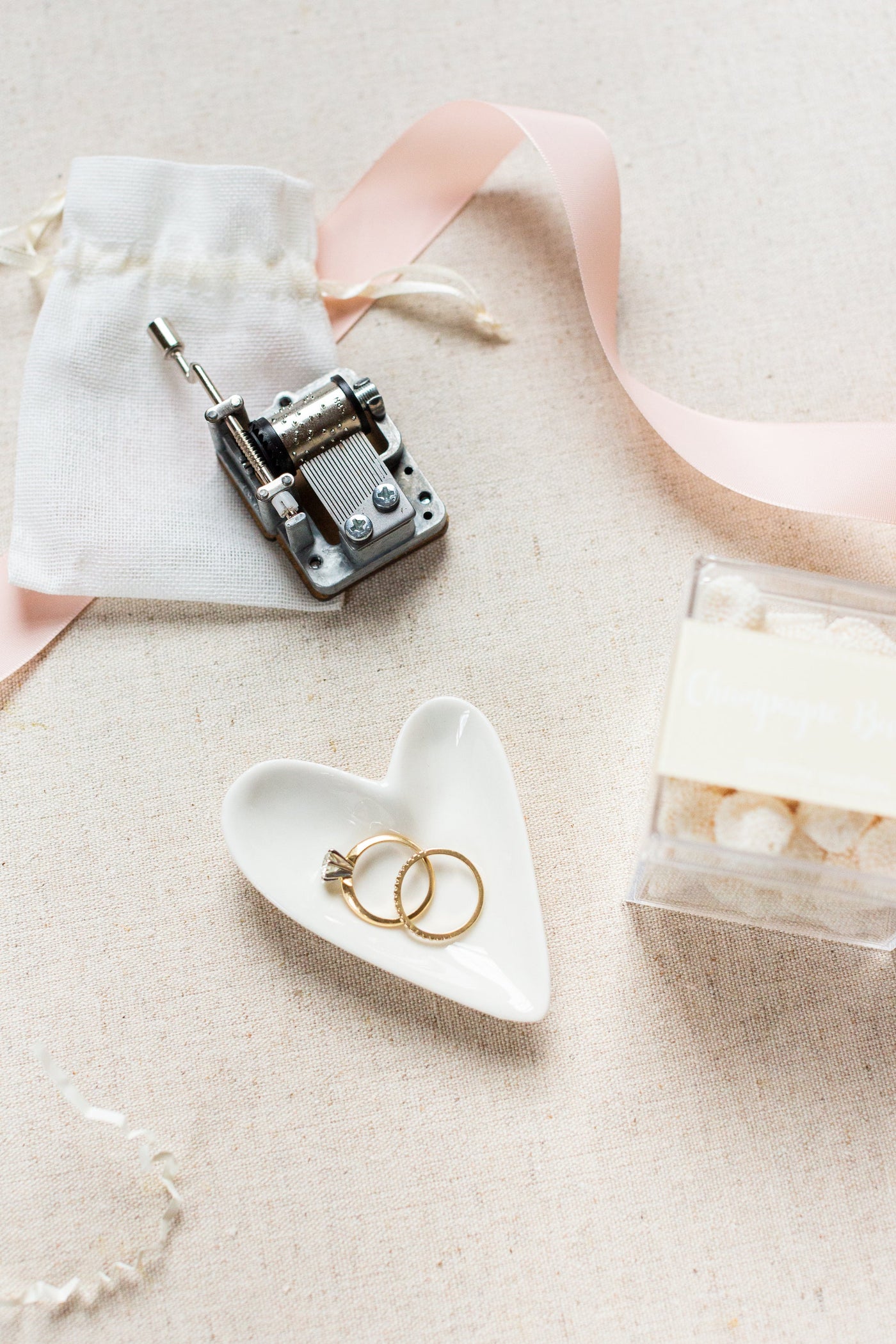 The LUX BOX Engagement Gift Box is an elegant choice, featuring a charming music box, two gold rings on a heart-shaped dish, a white pouch, and sugar cubes tied with a pink ribbon on beige cloth.