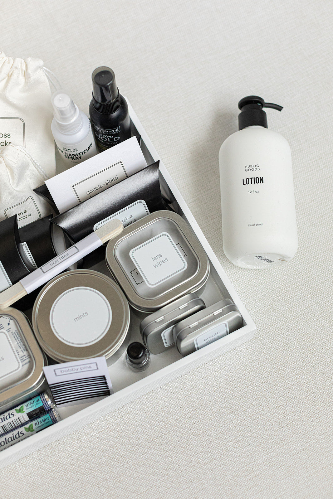 The HERS Bathroom Amenities Tray by LUX BOX displays toiletries like tins, spray bottles, stain removal wipes, and a toothbrush neatly arranged. A separate lotion bottle is gracefully placed on the side.