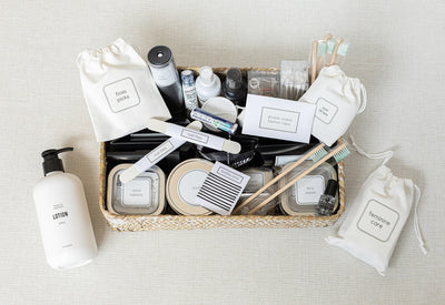 The Lux Box Co showcases a woven basket filled with toiletries like floss picks, cotton swabs, toothpaste tablets, and lotions. Perfect for corporate gifting, it includes two toothbrushes and a lotion bottle to complement this thoughtful selection.